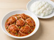 Ayam masak merah: chicken pieces in a thick red chilli and tomato sauce with onion rings and peas, with a plate of white rice