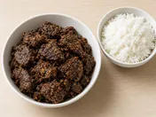Dark, dry beef rendang in a white bowl, with a small bowl of steamed rice beside it