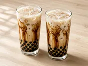 Two tall glasses of brown sugar boba milk tea with dark syrup streaks, tapioca pearls, ice and milk