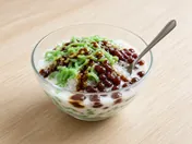 Cendol in a glass bowl: green pandan jelly, red beans, shaved ice, coconut milk and palm sugar syrup, with a spoon