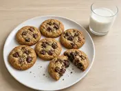 Chocolate chip cookies on a white plate with a glass of milk