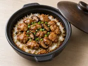 Claypot chicken rice: glazed chicken and shiitake mushrooms on rice in a black clay pot, topped with spring onion
