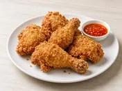 Golden, craggy crispy fried chicken pieces on a white plate with a small bowl of chilli sauce