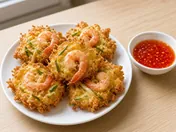 Golden, crispy cucur udang prawn fritters with whole prawns, chives and bean sprouts on a white plate, with a bowl of sweet chilli sauce