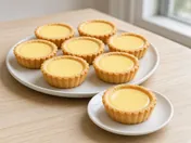 Hong Kong egg tarts with golden shortcrust cases and smooth, glossy yellow custard on a plate, one tart on a small plate in front