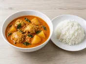 Kari ayam: chicken and potato curry with curry leaves in a white bowl, with a plate of white rice