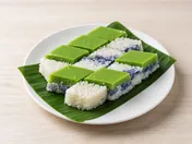 Squares of kuih seri muka with a green pandan custard top on white and blue glutinous rice, on a banana leaf