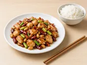Kung pao chicken with dried red chillies, spring onion and peanuts on a white plate, with rice and chopsticks