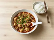 Mapo tofu with minced meat and spring onions in a white bowl, with a bowl of rice and chopsticks