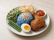 Nasi kerabu: blue rice topped with toasted coconut, with herb salad, long beans, a salted egg half, fried chicken leg, crackers and chilli dip