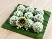 Green onde-onde balls rolled in grated coconut on a banana leaf, one bitten open to show the melted palm sugar