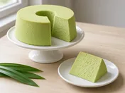 A tall pale green pandan chiffon cake on a cake stand with one slice cut out, the slice on a small plate showing the light, airy crumb, with pandan leaves
