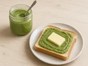 Green pandan kaya in a small glass jar with a spoon, next to slices of toast spread with kaya and butter