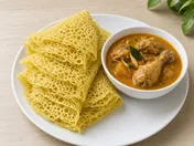 Folded yellow roti jala net crepes on a plate with a bowl of chicken curry