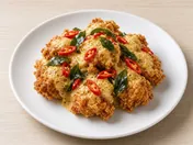 Salted egg chicken: crisp chicken pieces coated in golden salted egg yolk sauce with curry leaves and sliced chilli on a white plate