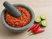Sambal belacan in a stone mortar with a pestle, with halved kalamansi limes and fresh red chillies beside it