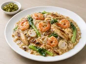 Wat tan hor: flat rice noodles in silky egg gravy with prawns, chicken, fish cake and choy sum on a white plate, with pickled green chillies