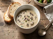 A bowl of creamy wild mushroom soup with slices of toasted garlic bread on a rustic wooden table